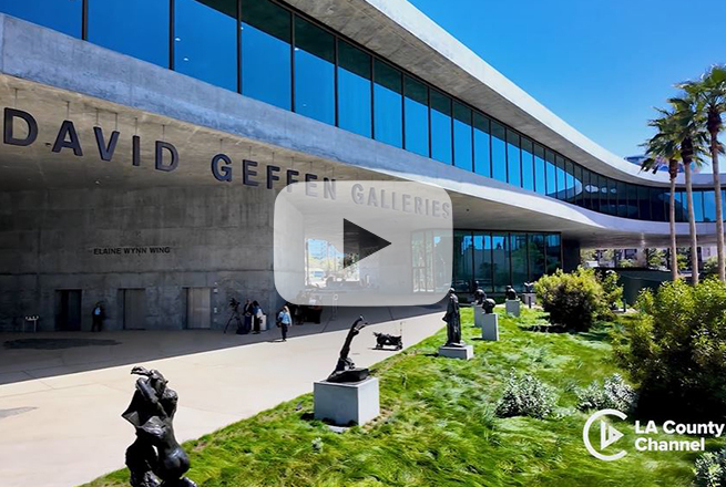 David Geffen Galleries building with glass windows, people walking outside, grass area with plants and palm trees, and art work