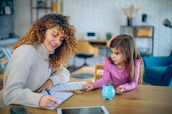 a woman in a gray sweater is writing on a piece of paper while a little girl in a pink shirt looks on