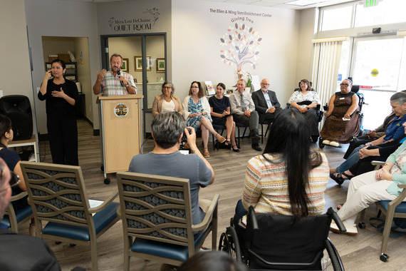 A diverse group of people sit at a launch event while a speaker talks at a podium.