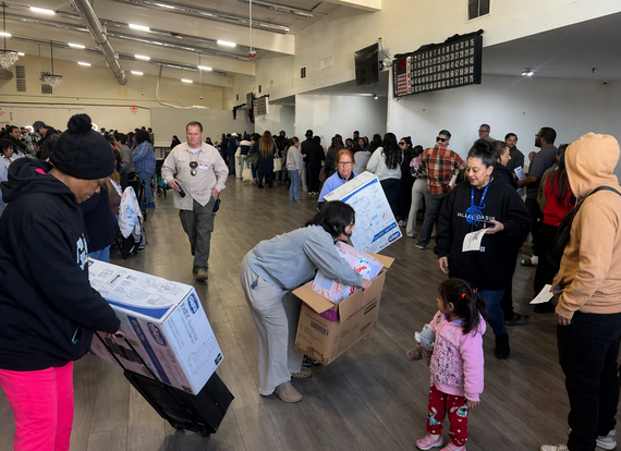 People stand in a large auditorium carrying items and talking to one another.