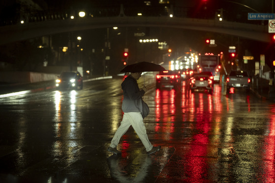 Male holding umbrella crossing the street at night with cars in the background