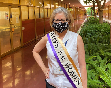 Registrar Lynda Roberts wears a sash that says Votes For Women