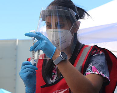 A person wearing protective equipment prepares a dose of the COVID-19 vaccine