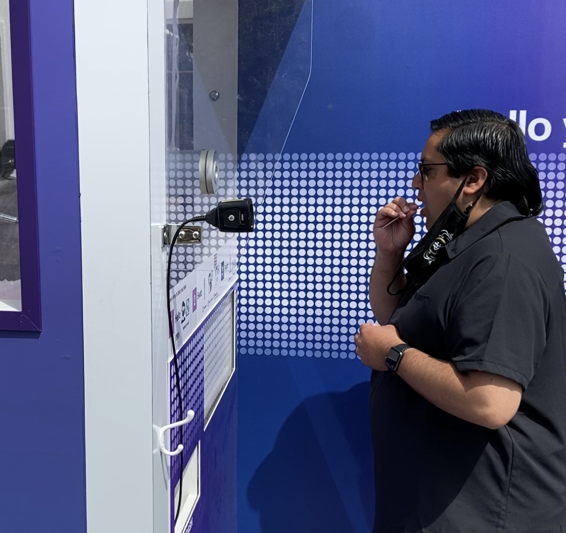null Man standing in front of a Curative testing kiosk, performing a self administered oral swab test