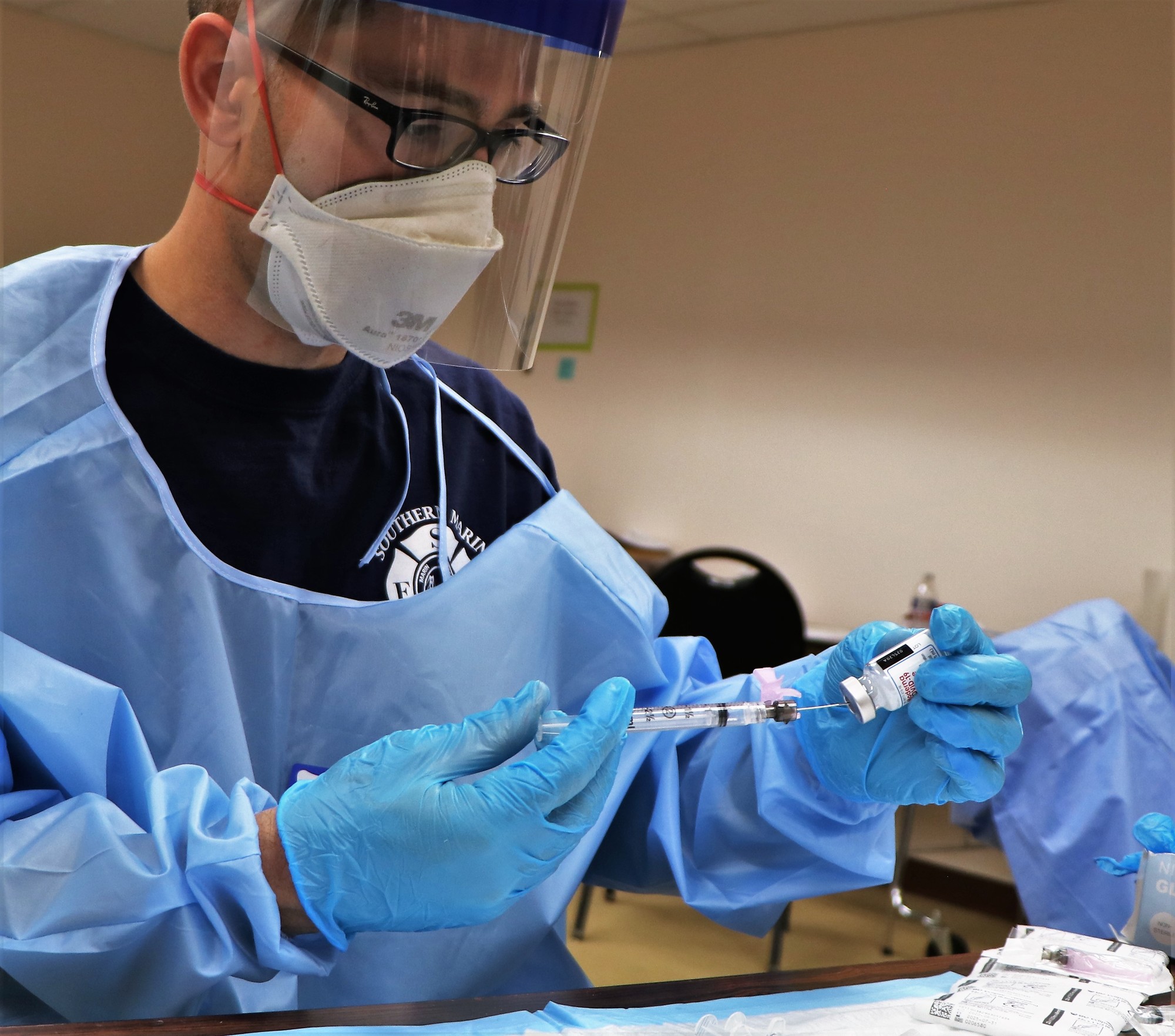 A male paramedic wearing protective gear loads syringes with COVID-19 vaccine doses.