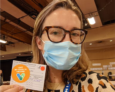 A woman named Alison Sexauer holds up her COVID-19 vaccination card
