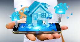 A hand holding a smart phone with a holographic image of a house on top.  Various icons for cloud, Internet, e-mail, and messaging surround the house.
