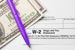 Two one-hundred dollar bills and a pen on top of a W-2 form.