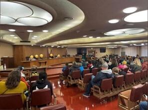 perspective from back of board chambers, students sitting in audience and on dais