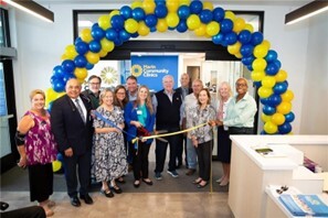 group smiling under yellow and blue balloon arch cutting ribbon