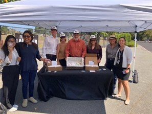 Supervisors in Nooner Lagooner hats under tent smiling toward camera with staff 
