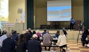Supervisor Sackett on stage next to projector speaking to seated audience 