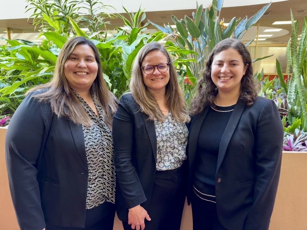 Crystal, Mary, and Julia smiling toward camera in front of plants in hallway of Civic Center