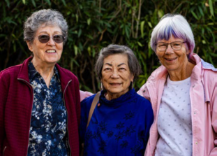 Three older women who deliver meals to other older people pose and smile.