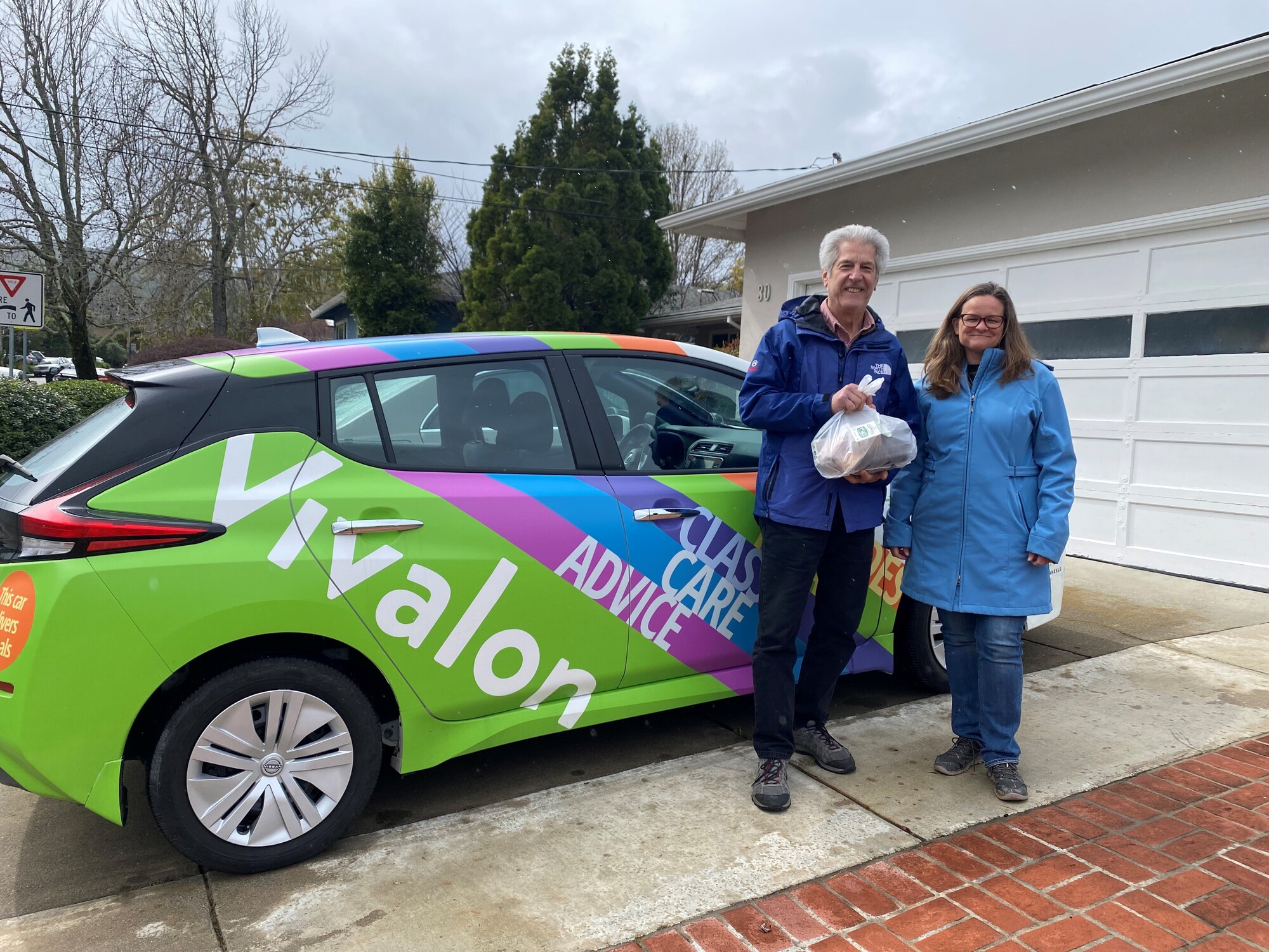 Mary and volunteer holding meal in front of Vivalon car