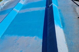 A closeup view of the paint on the Civic Center roof, part cleaned and bright blue and part dirty and gray.