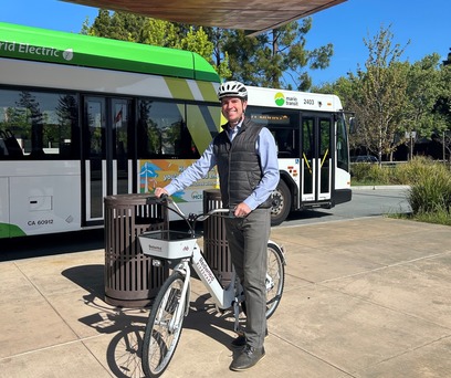 Supervisor Lucan on a bicycle at a bus stop in Novato.
