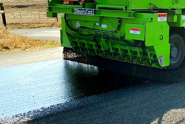 A closeup view of a road getting repaved by a piece of heavy machinery