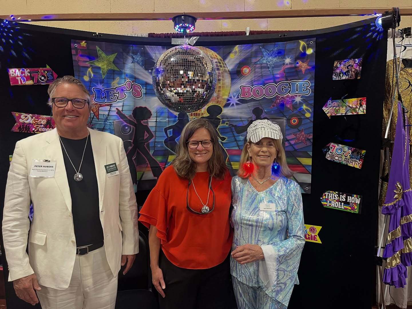 Mary smiling with Commission on Aging Commissioners Peter and Joan in front of disco backdrop