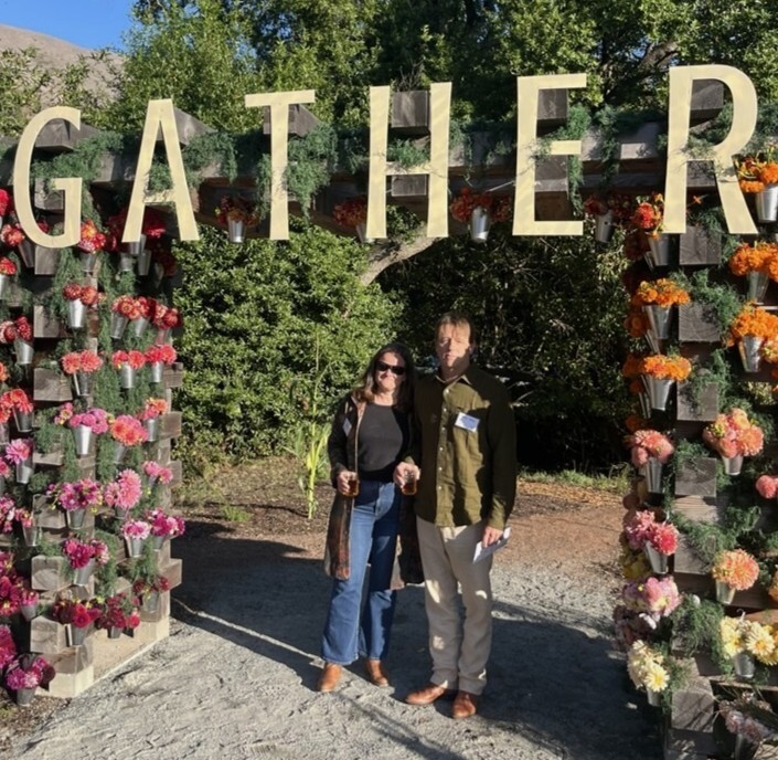 Mary and Shawn smile under floral archway with gather spelled out above
