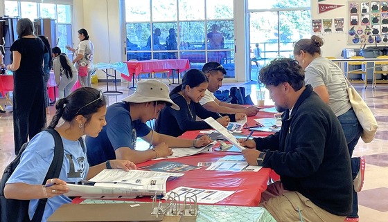 Several young people sit at a table and read materials about the Participatory Budgeting voting process.