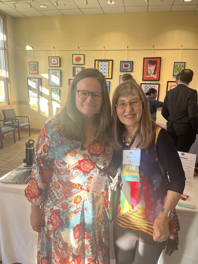 Mary and Jana smiling in Mill Valley Community Center in front of wall of art