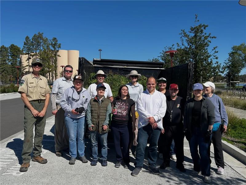 Group photo smiling in front of back of Parks truck filled with weeds with auditorium in background