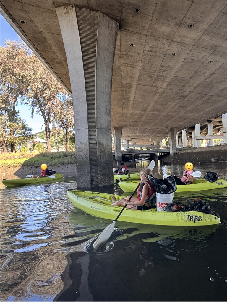 Kayaking under bridge with trash bins in back of kayaks