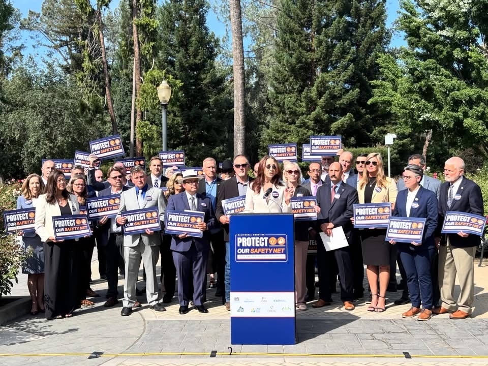 County Supervisors standing together holding blue protect our safety net signs at press conference