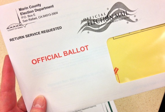 A person's hand is holding an envelop that contains an election ballot.