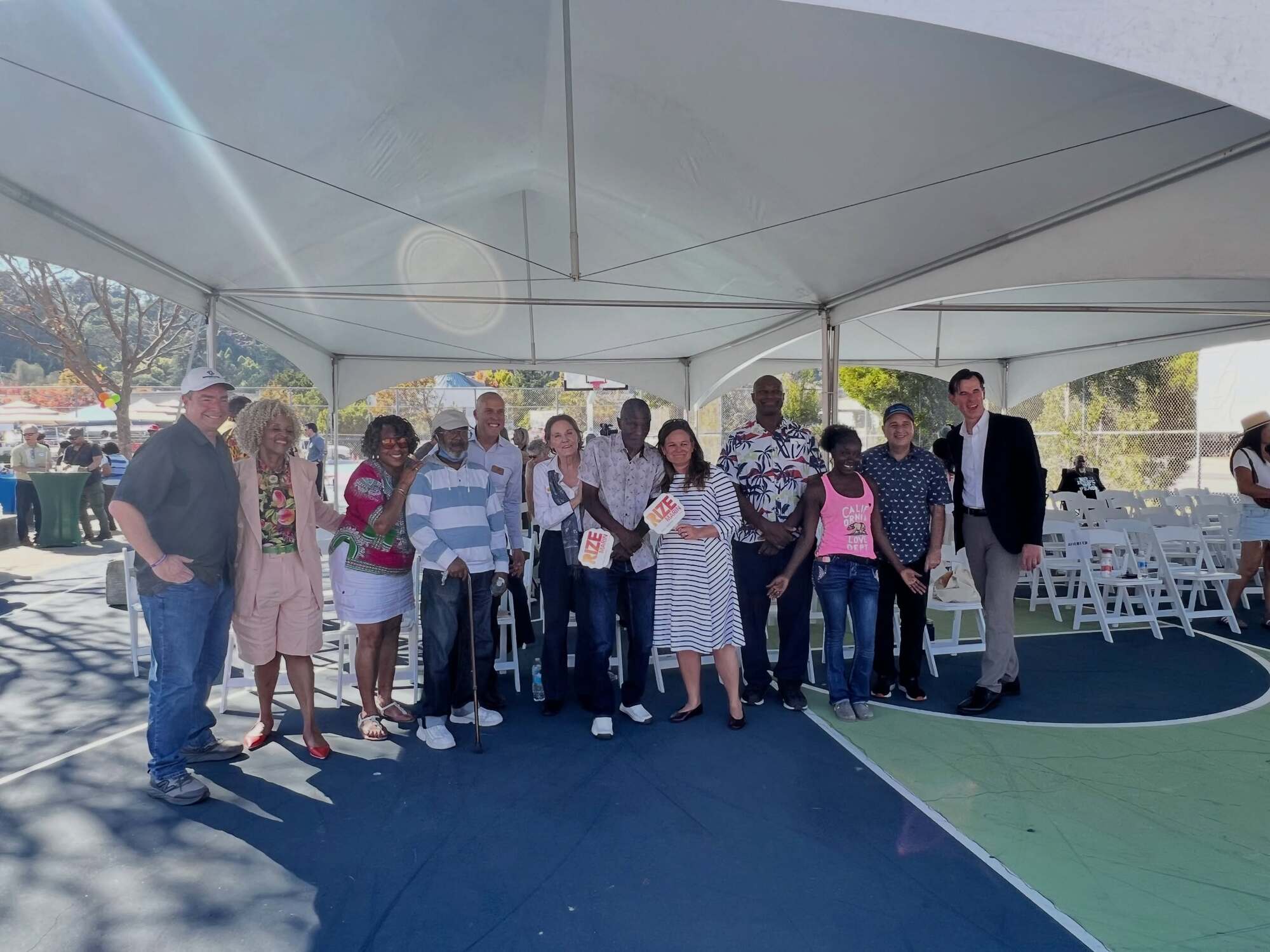 group gathered smiling under tent including Mary and elected officials and staff who support the project