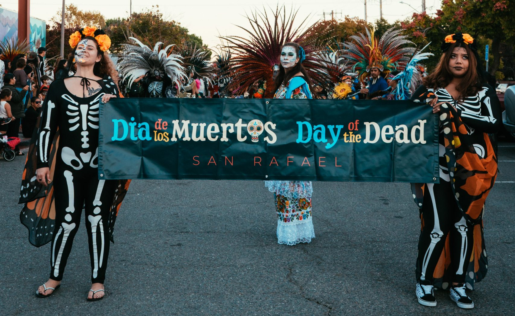 Dia de los Muertos Banner held by procession members wearing decorative skeleton outfits