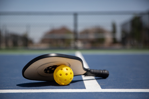 Image of blue pickleball court with racket and yellow ball on the ground.