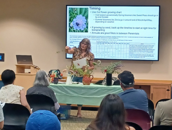 Photo of Master Gardener Laura Westley showing cut flowers to an audience