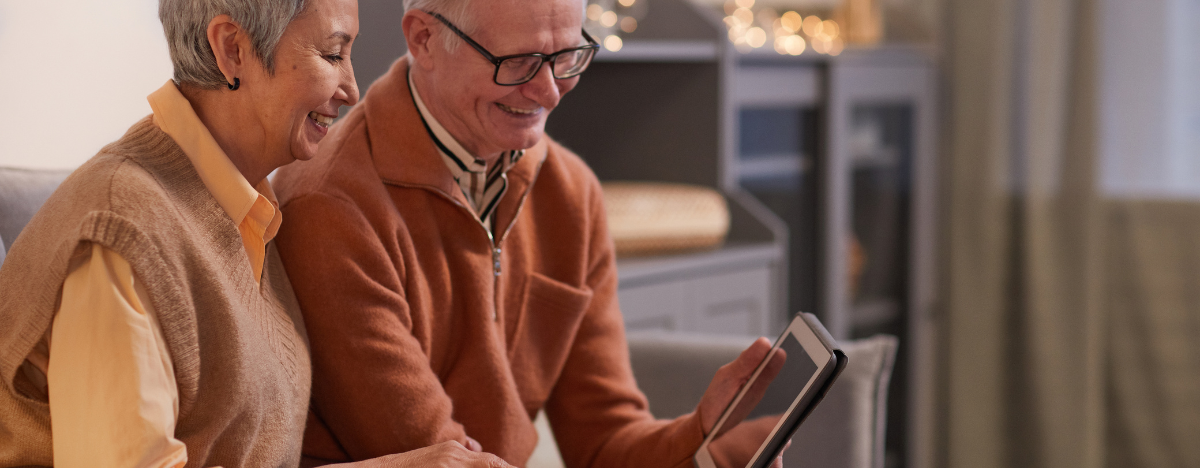 Photo of two seniors looking at an iPad while smiling