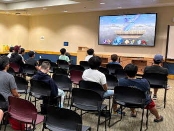 Photo of participants at the Super Smash Bros Infinite tournament watching a match on the TV