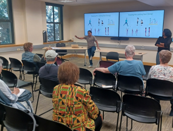 Photo of a group of seniors watching a presenter demonstrate strength building exercises