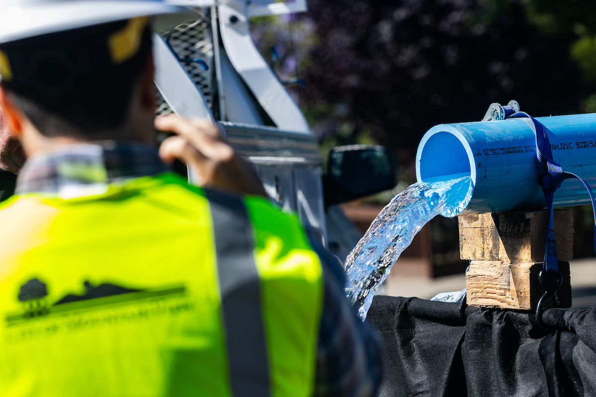 Image of water coming out of a blue pipe as an employee in a neon yellow vest watches