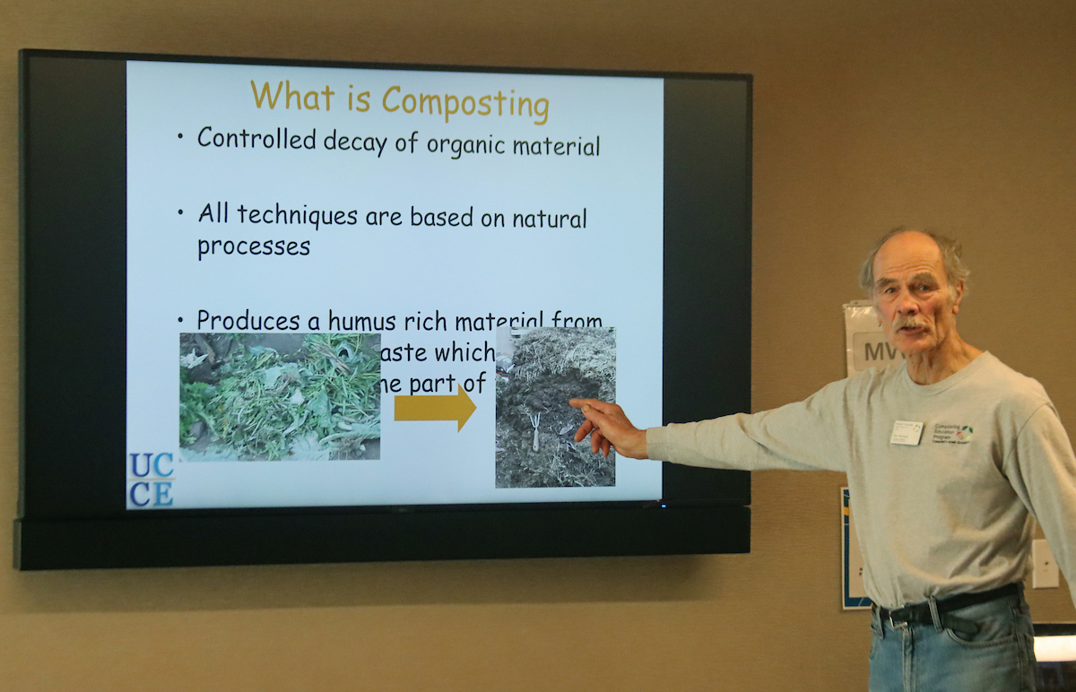 Photo of a man giving a presentation that says on the screen, What is composting?