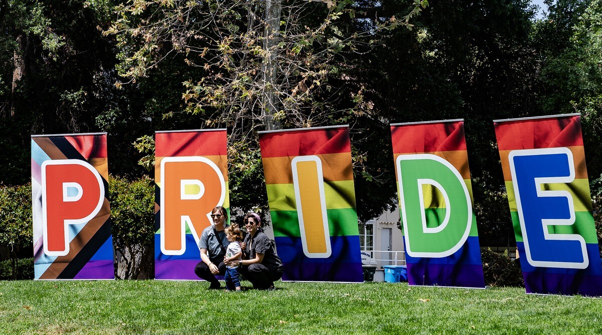 A family taking a photo in front of large, colorful P R I D E letters