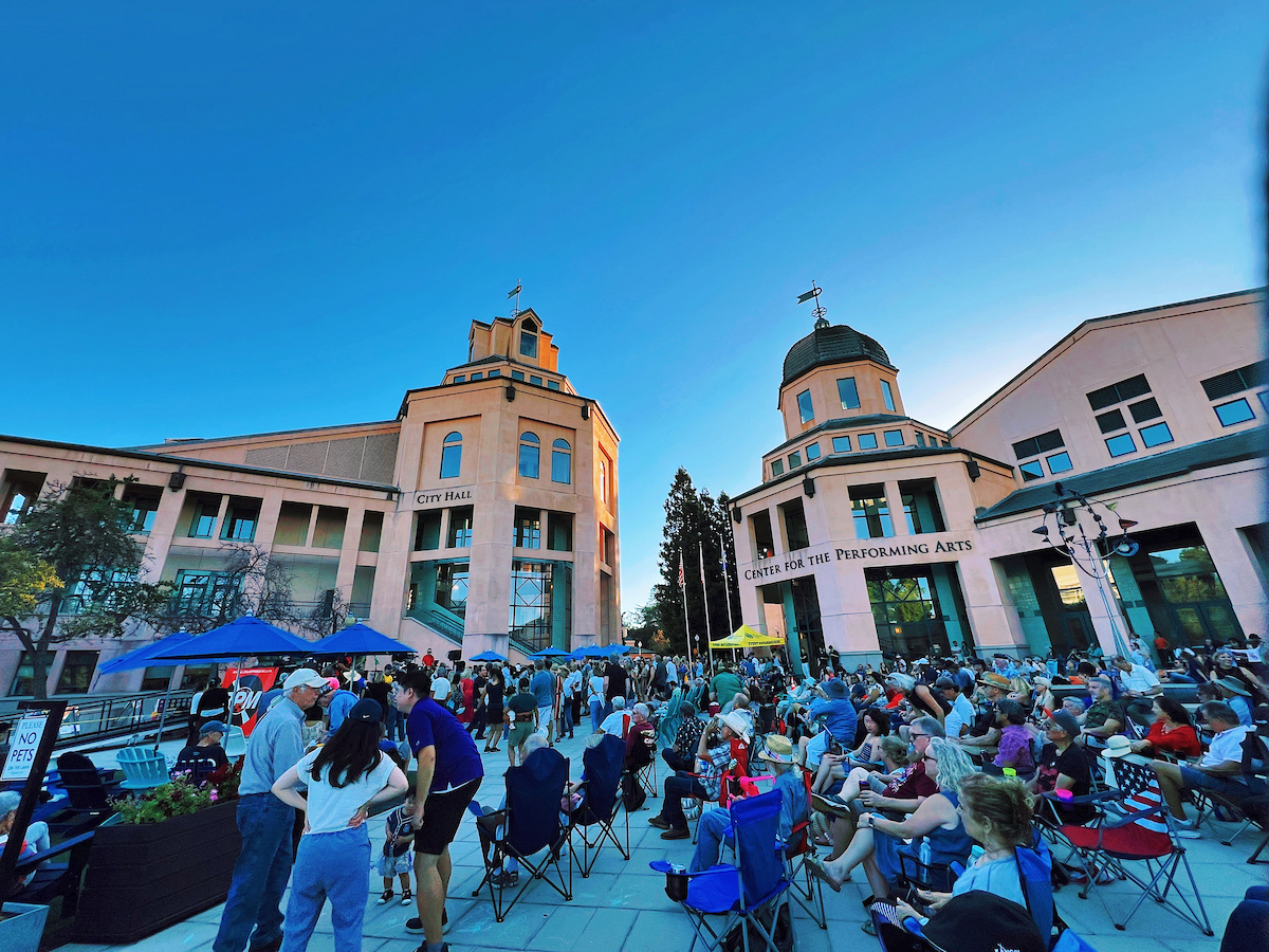 A diverse group of people sitting in lawn chairs at the Civic Center Plaza watching a concert