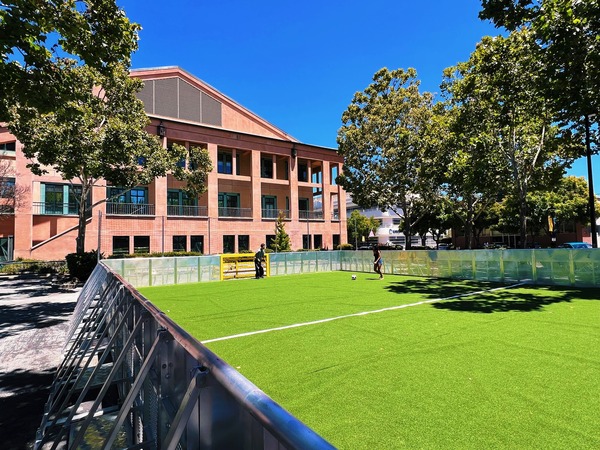 Two children playing soccer on a mini pitch with City Hall in the background