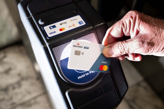 A hand holds a credit card against a sensor to pay for transit.