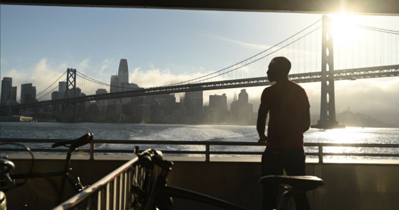 Man watches the Bay Bridge from a ferry next to several parked bikes.