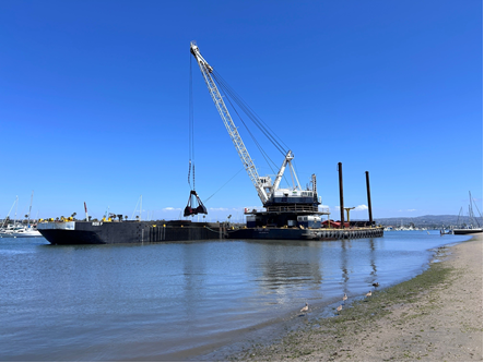 Ocean dredger scooping a large pile of debris into a waiting tow vessel