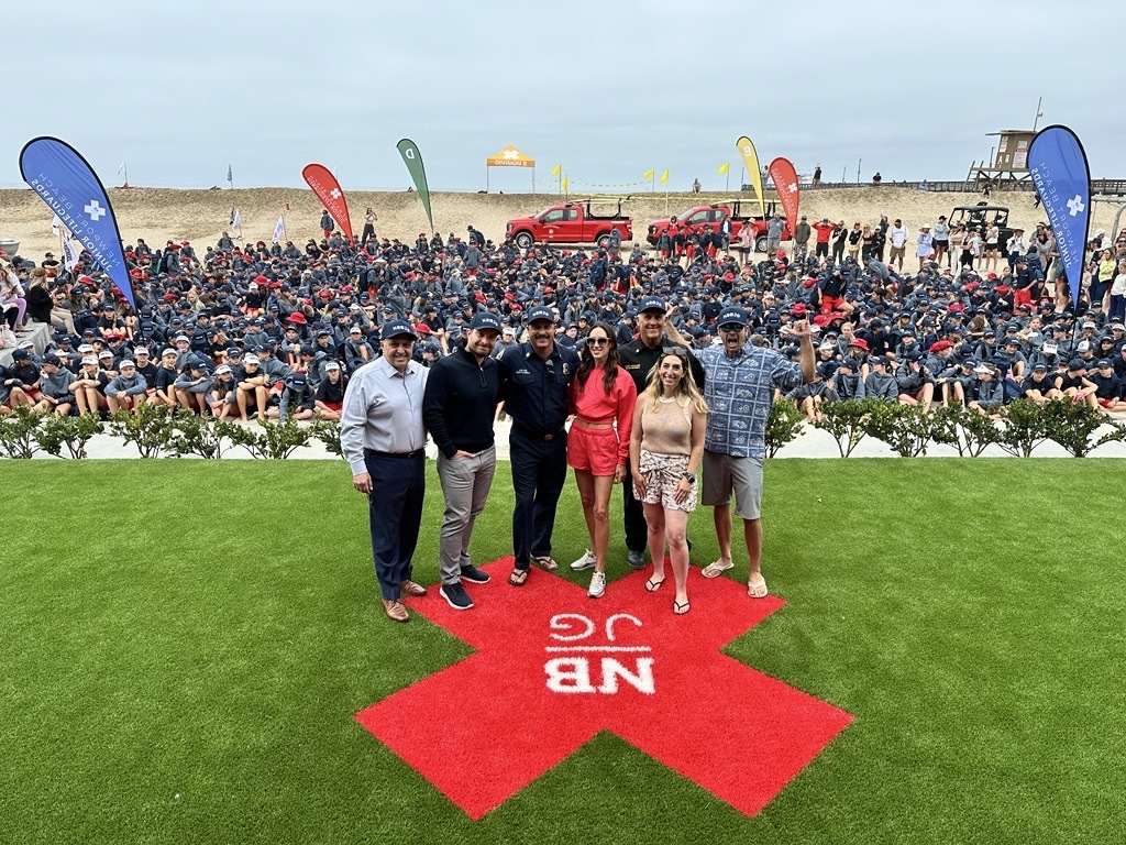 Group photo of Newport Beach leaders at the beach, with hundreds of Junior Guards gathered behind them during the opening event. 