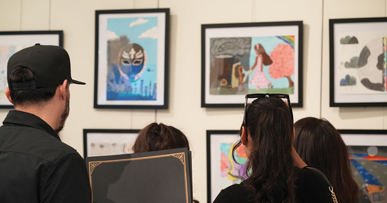 A group of four people looking at student artwork in the Youth Art Month exhibition