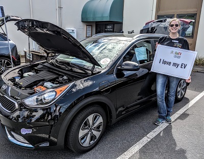 Woman with sign "I love my EV!" standing in front of a black EV.