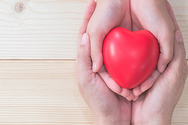 Photo of an adult and child's hands cupping a heart shaped object. 