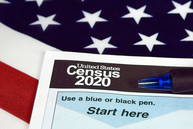 Photo of a pen and paper reading "United States Census 2020" laying on top of an American flag.